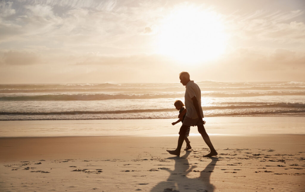 Man and grandchild walk the beach at sunset